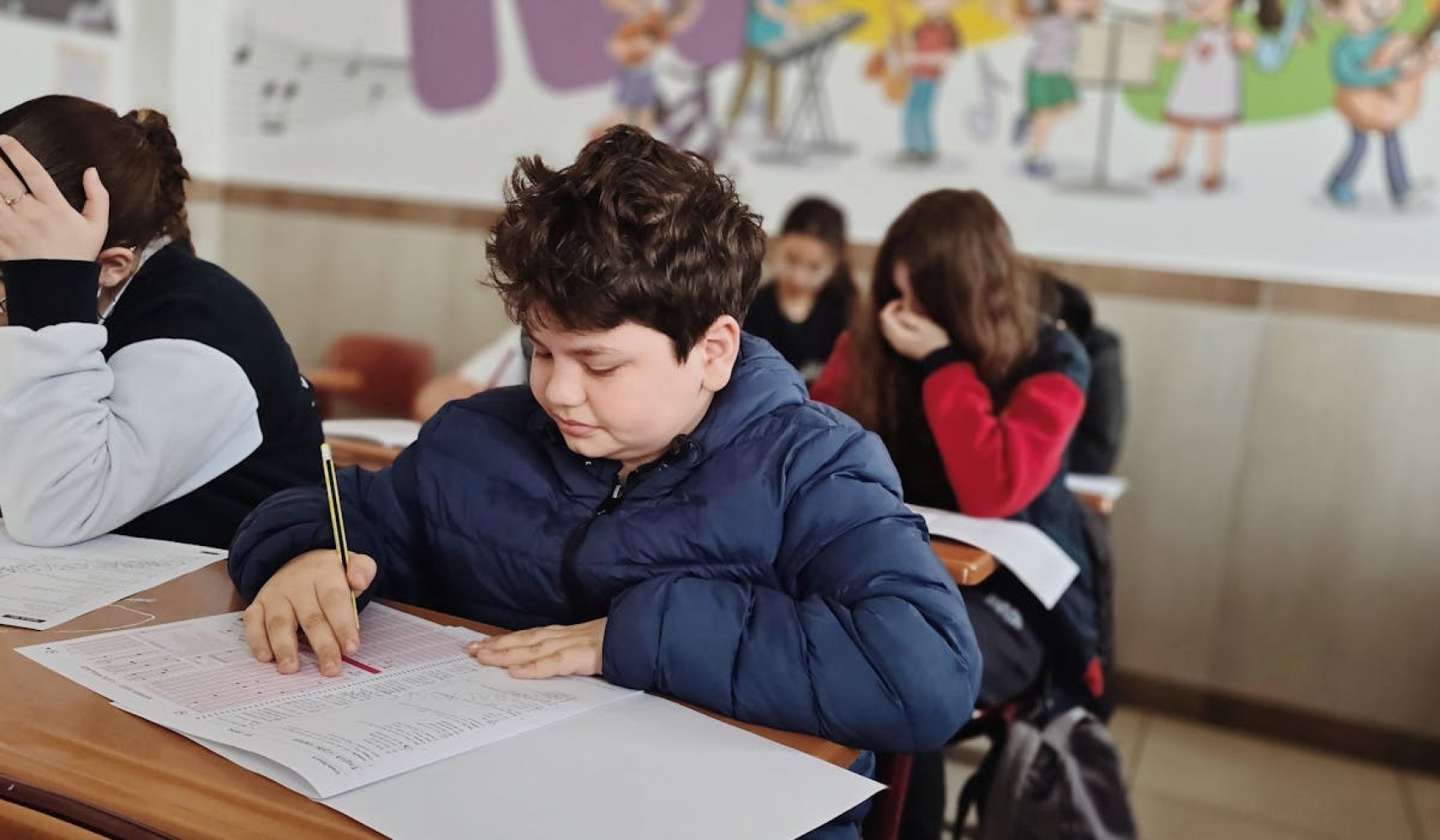 Grupa uczniów w sali egzaminacyjnej skupiona nad arkuszami maturalnymi